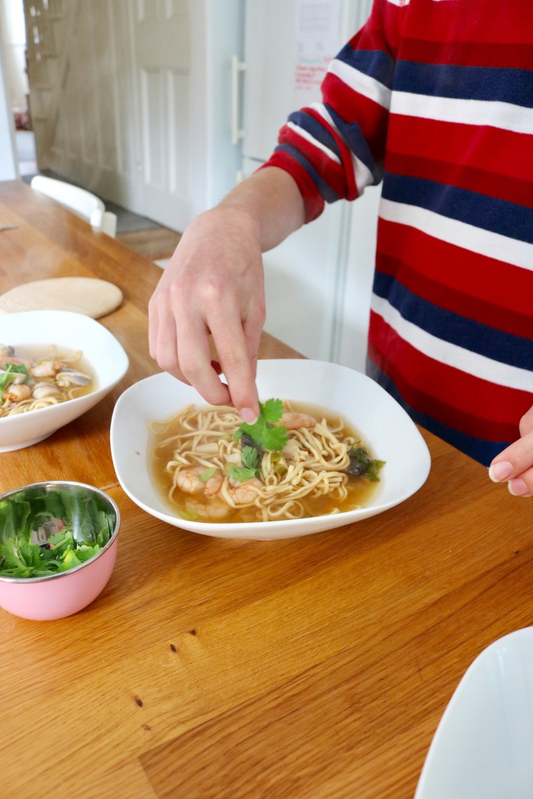 Coriander garnish being put on tom yum prawn noodle soup