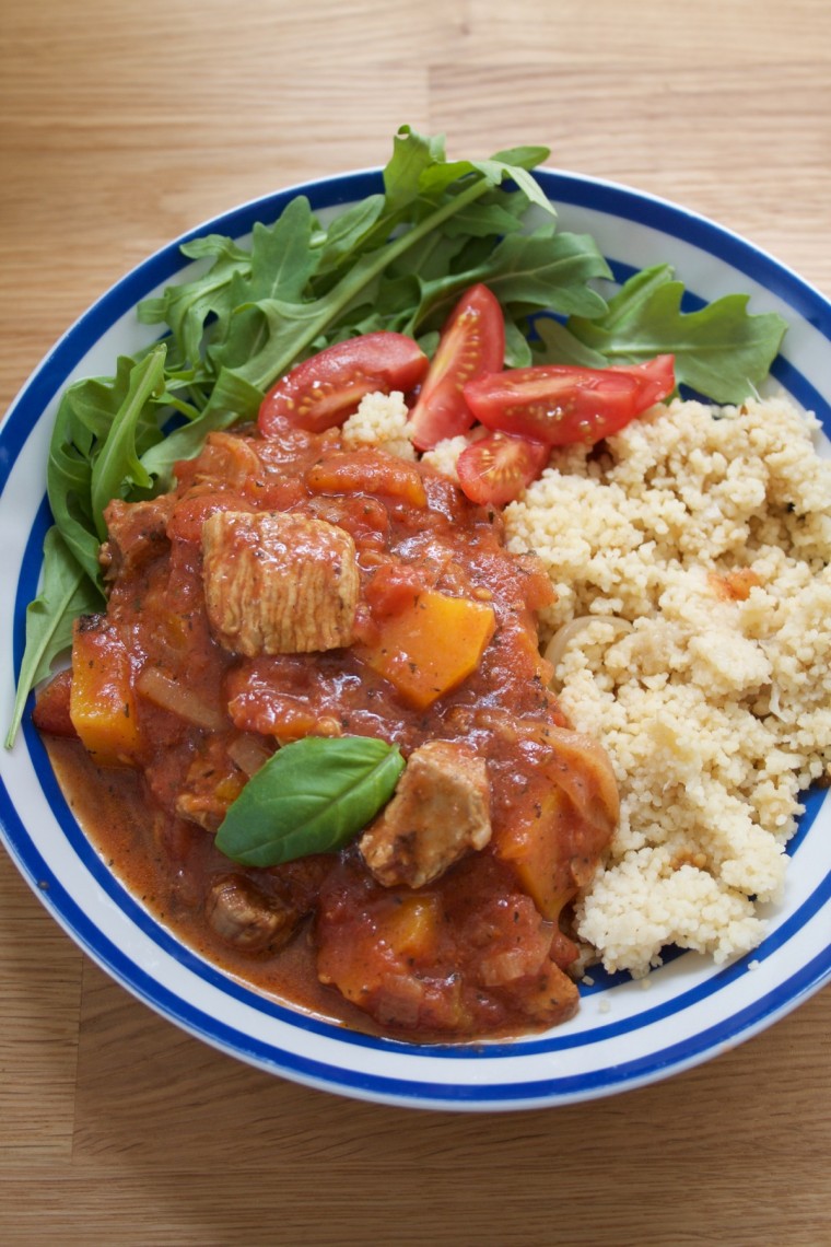 Turkey Thigh Tagine stew served in a blue stripey bowl alongside rocket and cous cous - portrait