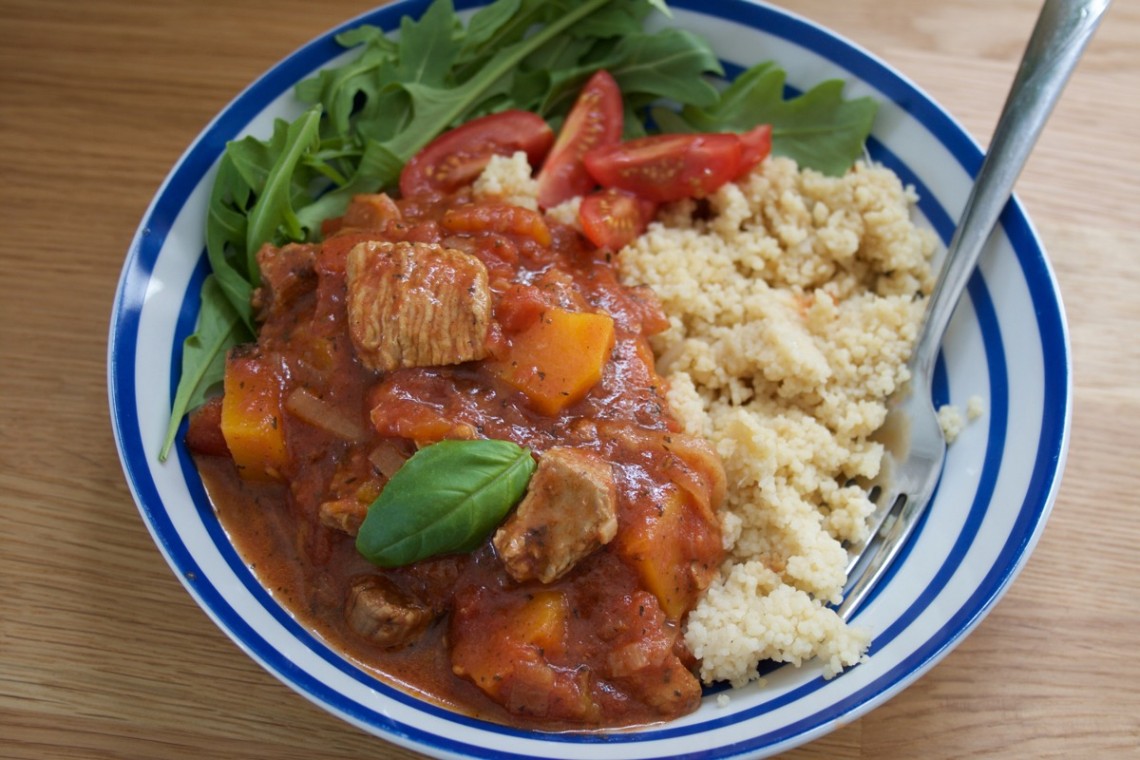 Turkey Thigh Tagine stew served in a blue stripey bowl alongside rocket and cous cous - landscape