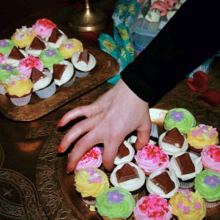 A hand reaches in to choose from a plate of colourful mini cupcakes