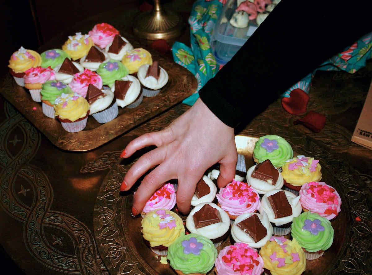 A hand reaches in to choose from a plate of colourful mini cupcakes