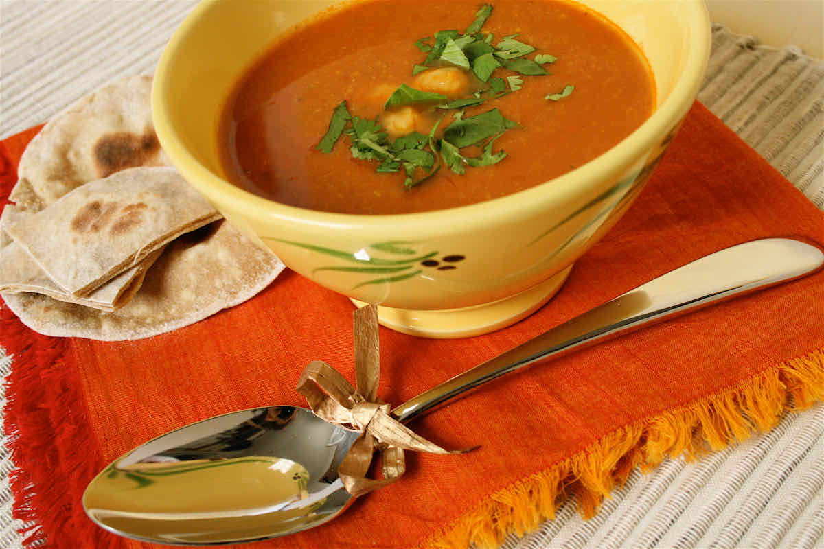 Spicy Chickpea Soup recipe served in yellow bowl with chapattis in background and orange napkin underneath