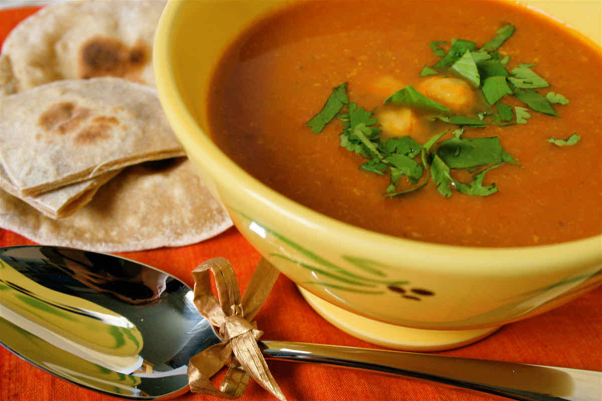 Spicy Chickpea Soup recipe served in yellow bowl with chapattis in background