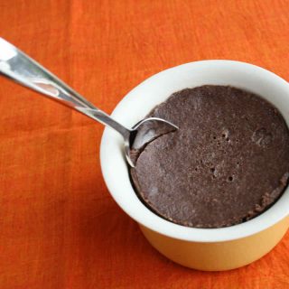 A ramekin of chocolate custard with spoon sticking in, upon an orange napkin background.