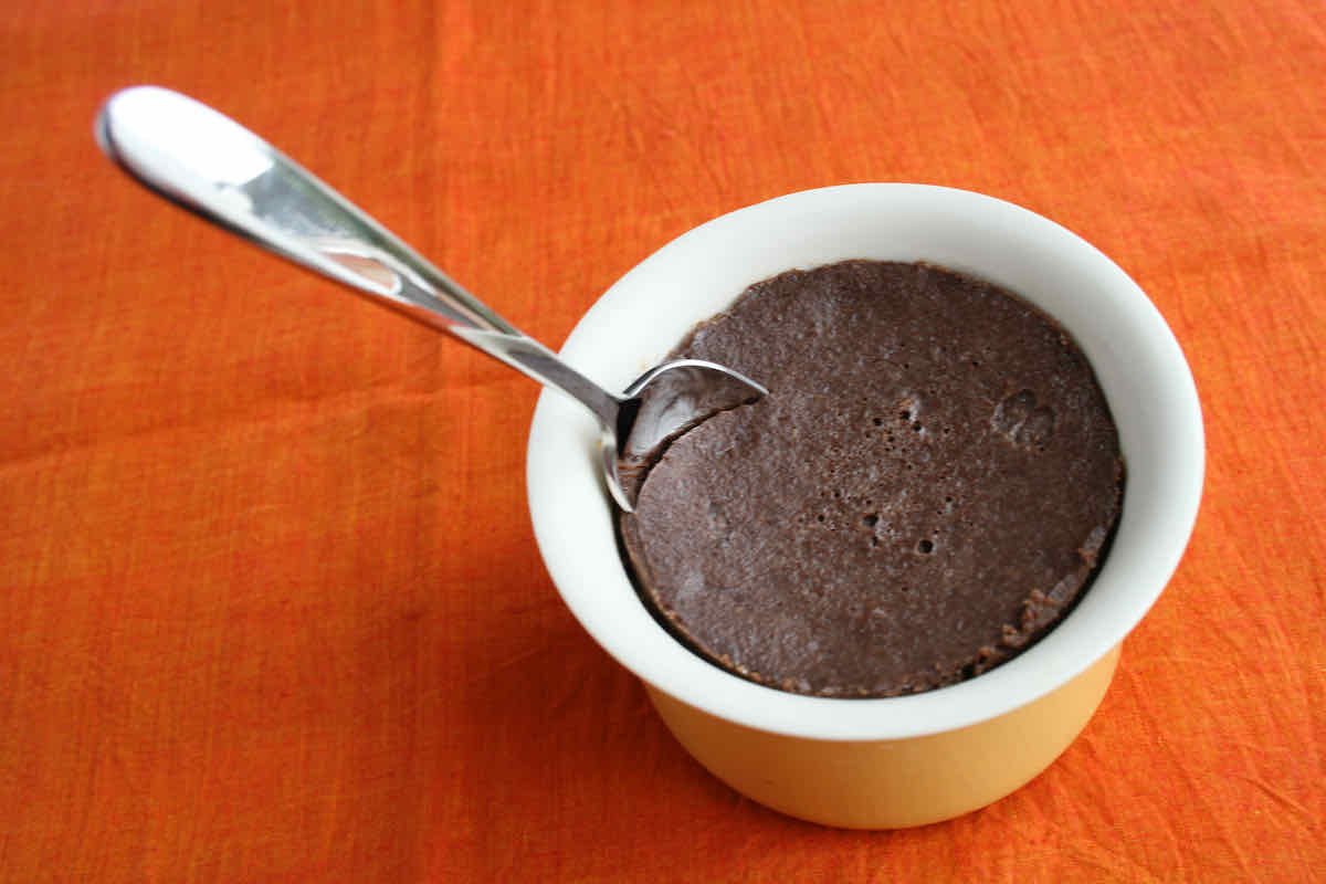 A ramekin of chocolate custard with spoon sticking in, upon an orange napkin background.