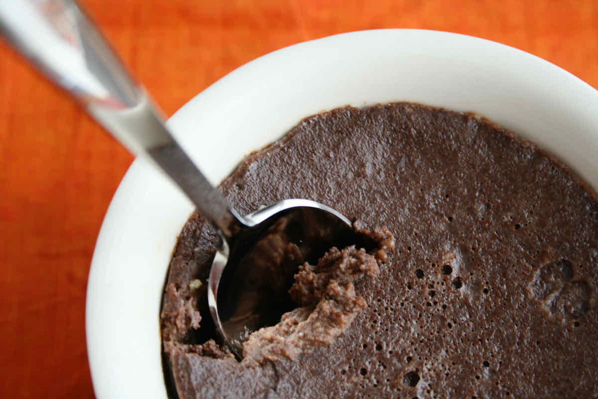 A ramekin of chocolate custard with spoon sticking in, upon an orange napkin background.