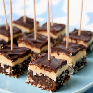 Bitesize Nanaimo bars cut into chunks and speared with cocktail sticks on a light blue plate.