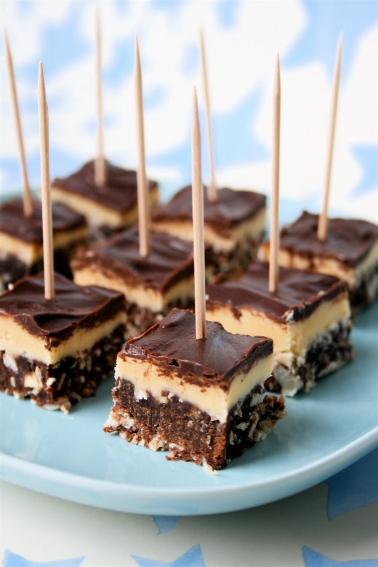 Bitesize Nanaimo bars cut into chunks and speared with cocktail sticks on a light blue plate.