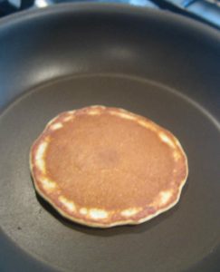 Cooked scotch pancake after it has been flipped over showing golden underside.