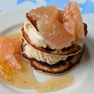 Stack of small Scotch pancakes layered with ice cream, grapefruit segments and swirl of pale orange sauce.