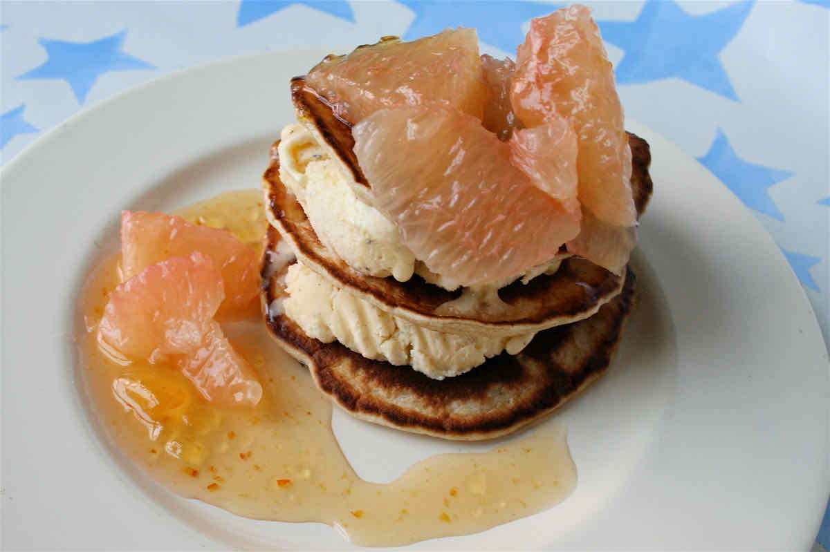 Stack of small Scotch pancakes layered with ice cream, grapefruit segments and swirl of pale orange sauce.