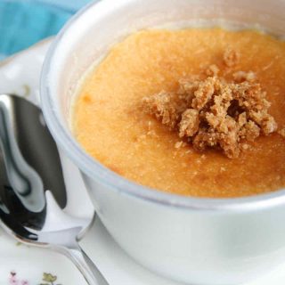 Silver ramekin of golden lemon custard dessert covered with biscuit crumbs; served on a vintage chintz plate with small serving spoon