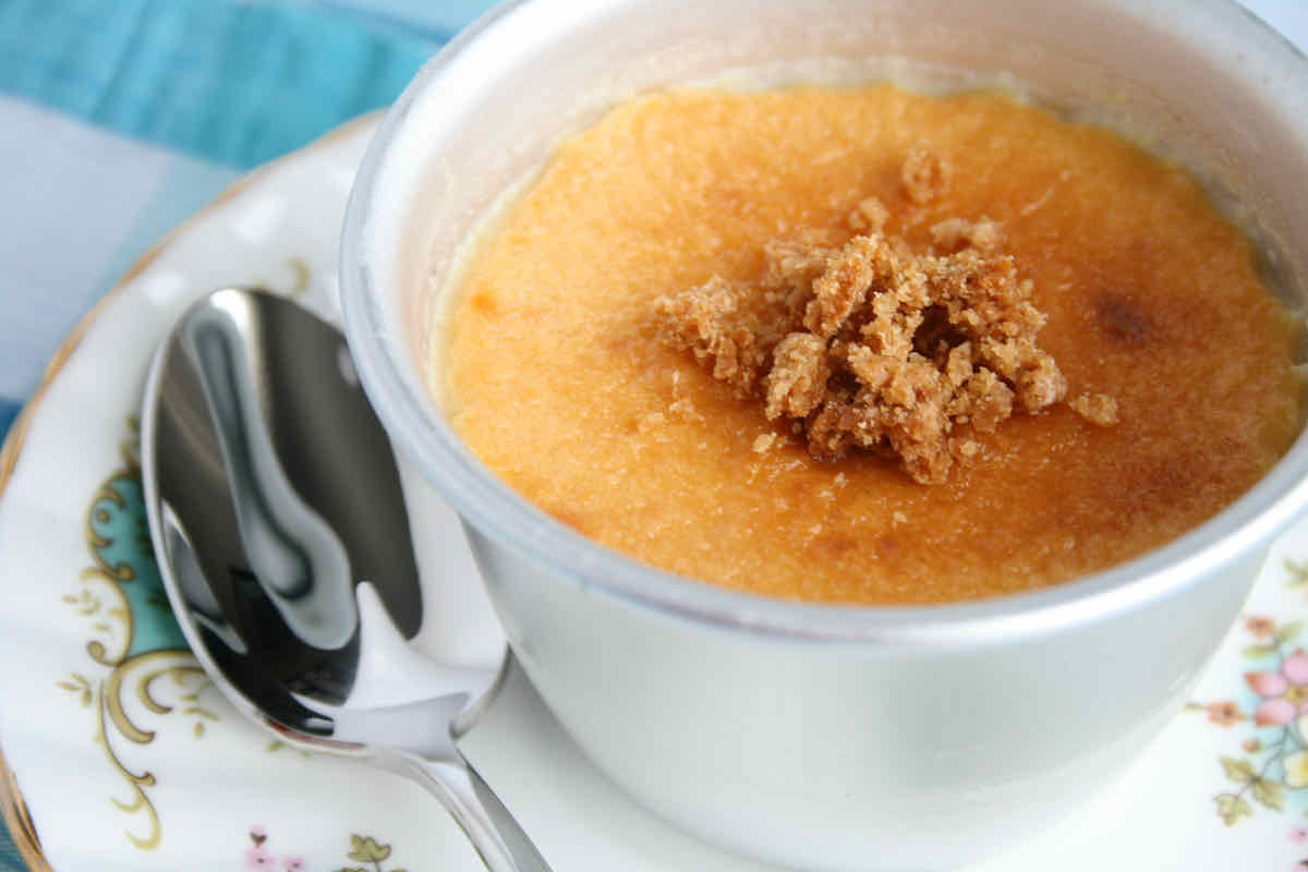 Silver ramekin of golden lemon custard dessert covered with biscuit crumbs; served on a vintage chintz plate with small serving spoon