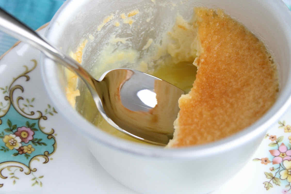 A silver ramekin of lemon custard dessert, half eaten with spoon 