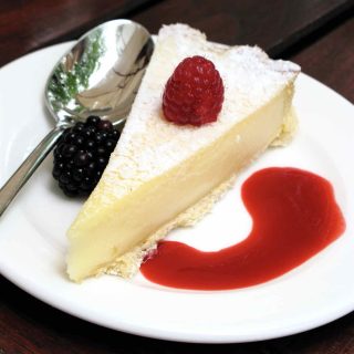 Food Blogger Connect at The Hempel 2010: A triangle of cheese cake with a raspberry on top and a blackberry and swirl of raspberry sauce either side on a white plate with a spoon.