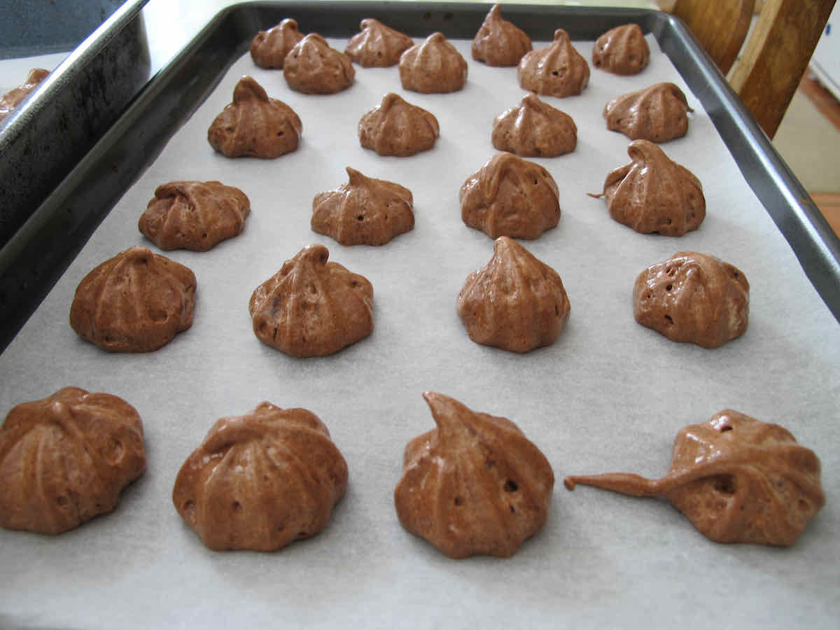 Baking tray of piped chocolate meringues on sheet of baking paper about to be baked