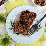 Apple Loaf Cake with Nuts and Chocolate: from above, a white plate with dessert fork, rectangle slice of loaf cake, on a surface with green flowers and paper napkin.