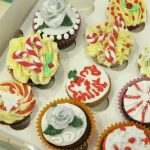 Mich Turner Cupcake Class: Selection of hand decorated Christmas themed cupcakes with glittery and messy decoration in a cardboard box.