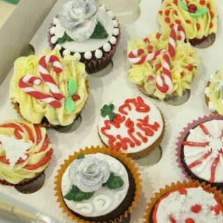 Selection of hand decorated Christmas themed cupcakes with glittery and messy decoration in a cardboard box.