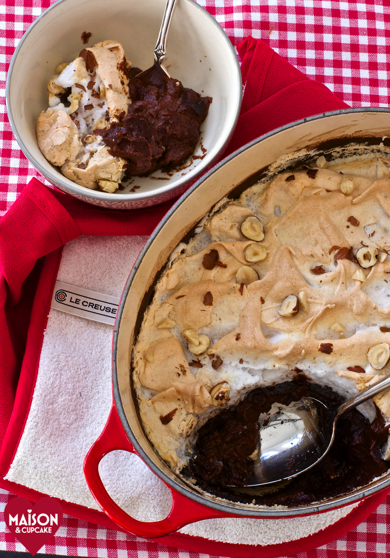 Nutella Semolina Meringue Pudding, seen from above, in an oval shaped red casserole dish, on a red gingham cloth. A serving sits in a small dish to the side.