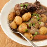 Crockpot beef on the bone stew slow cooker recipe served in white bowl with potatoes, carrots, onions and gravy.