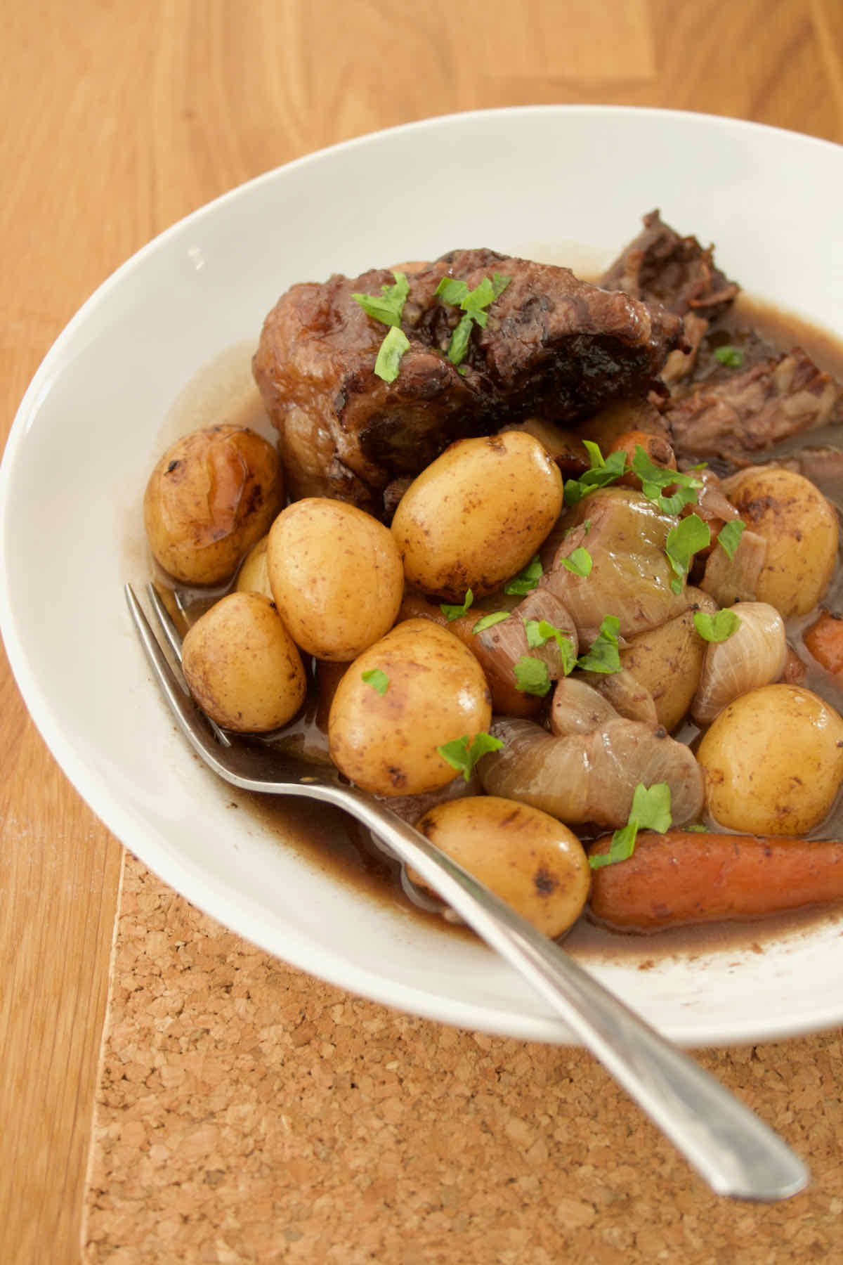 Crockpot beef on the bone stew slow cooker recipe served in white bowl with potatoes, carrots, onions and gravy.