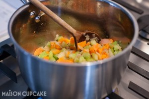 Soffrito of chopped onions, celery and carrots being fried in a stainless steel saucepan on the gas hob.