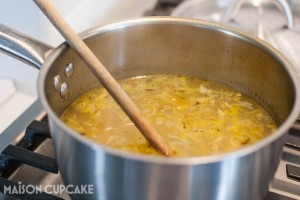 Golden vegetable stock in a stainless steel pan with wooden spoon.