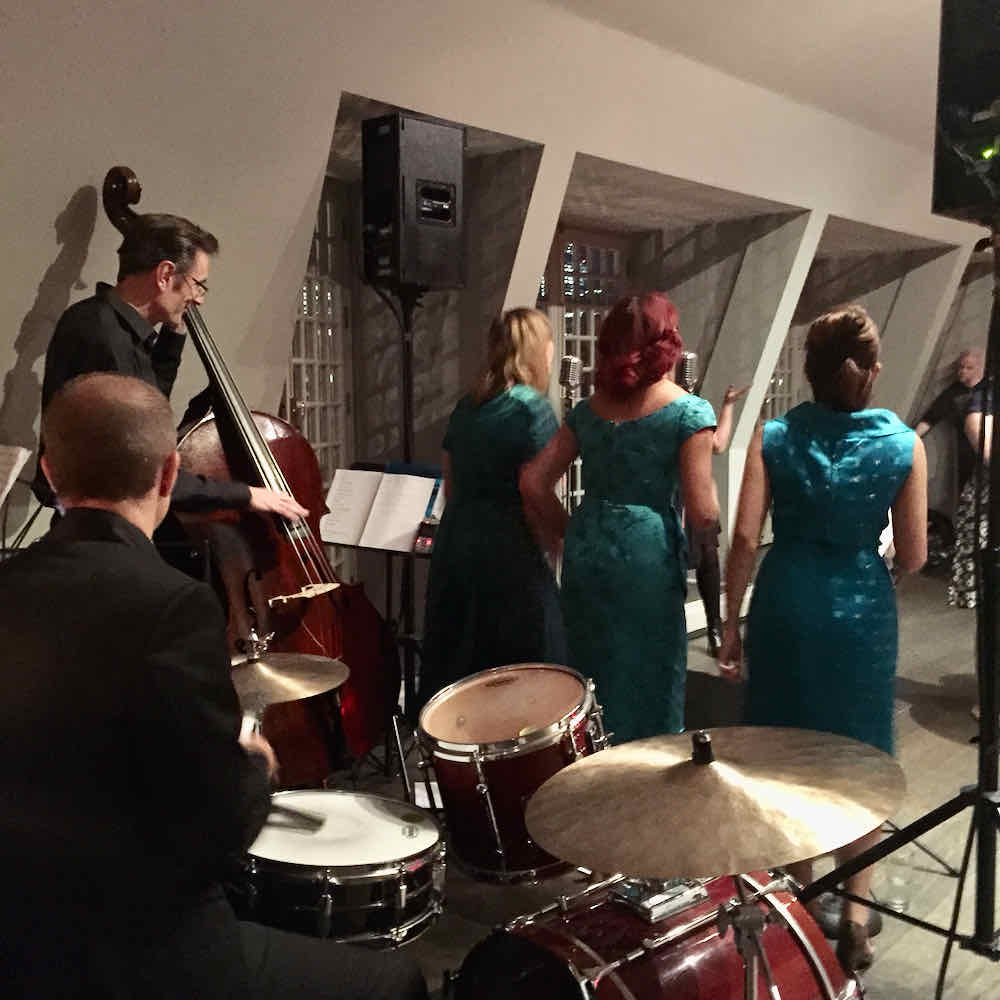 Harmonious girl trio seen from behind, performing with double bass player and drummer at Russell Hobbs 60th anniversary event