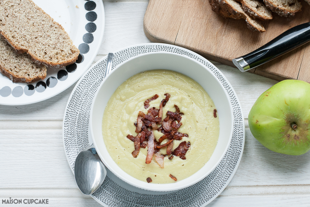 Edamame bean soup with Bramley apples and bacon - in a white bowl, slices of soda bread and a wooden board lie part in shot. A whole Bramley apple is to the right. 