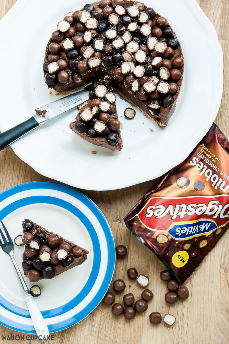 Chocolate Quark Cheesecake - Easy No Bake Recipe. Seen from above, chocolate cheesecake wtih crunchy biscuit pieces. A slice has been cut away and sites on a stripey blue plate with a fork. A bag of McVities Nibbles to the side.