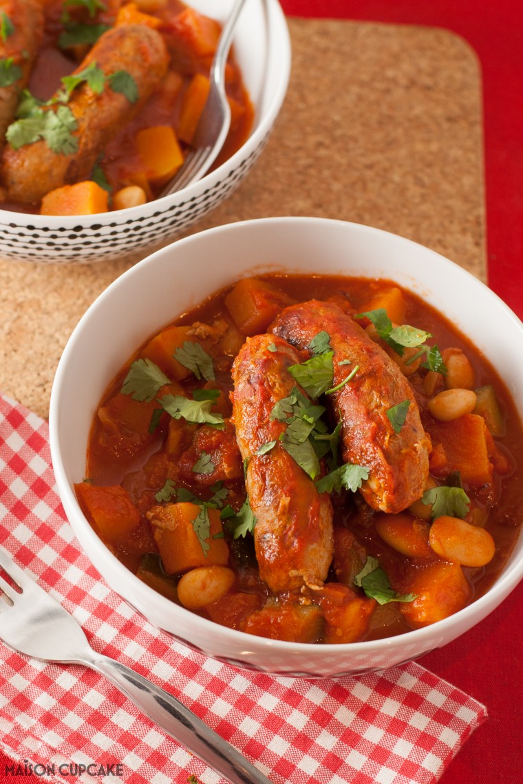 Low fat sausage and bean casserole in a white bowl; in tomato sauce upon a red gingham napkin with a fork.