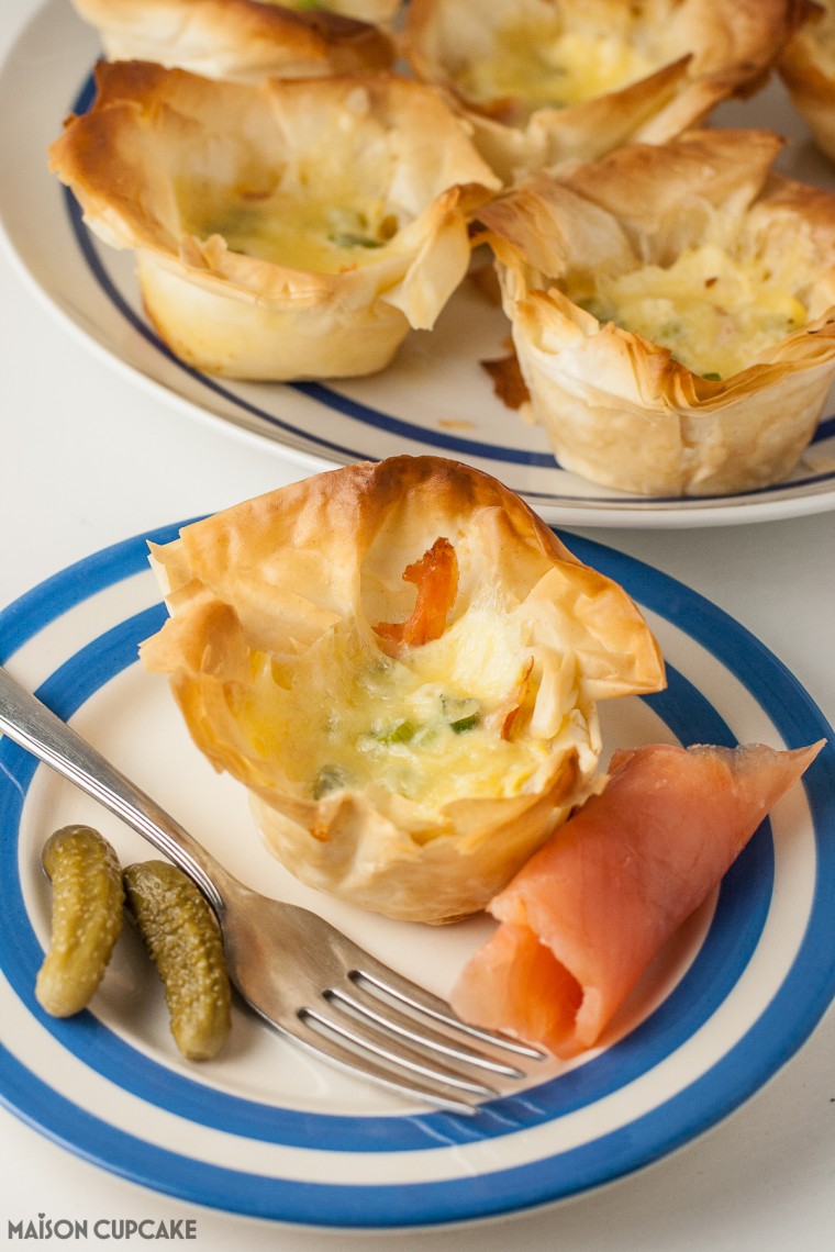 Salmon Filo Quiches Recipe, a single mini quiche on a blue stripey plate with cornichons and a piece of smoked salmon.