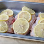 Oven dish containing lemon slices on chicken supreme pieces before cooking