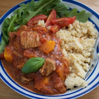 Turkey Thigh Tagine stew served in a blue stripey bowl alongside rocket and cous cous - landscape