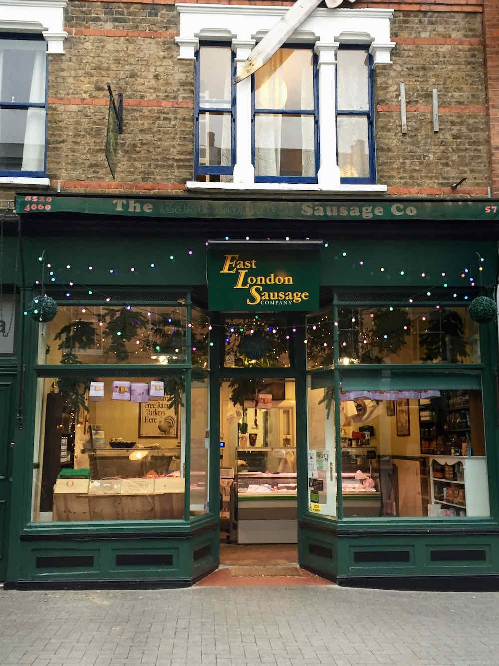 East London Sausage Company butcher shop front at Christmas with fairy lights and 'Fresh turkeys here' poster, Walthamstow Village, London