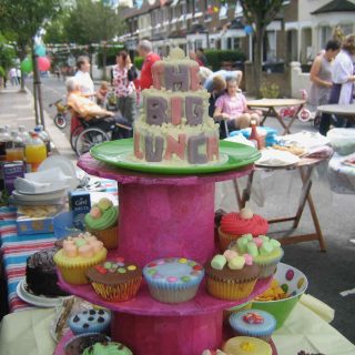 A street party scene with bunting and a cake saying The Big Lunch in foreground on a pink cake stand. Photo copyright Sarah Trivuncic 2009, all rights reserved, no reproduction without permission.