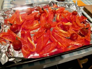 Red pepper strips and cherry tomatoes on a baking sheet lined with foil.