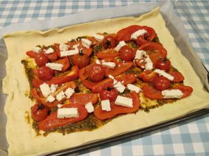 Rectangle of puff pastry covered in red pepper strips, tomatoes and feta before being baked in the oven.