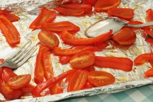 Lightly roasted red pepper strips and baby tomatoes upon a baking sheet lined with foil.