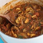 Casserole dish of richly coloured leftover lamb curry with mushrooms.