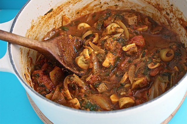 Casserole dish of richly coloured leftover lamb curry with mushrooms.