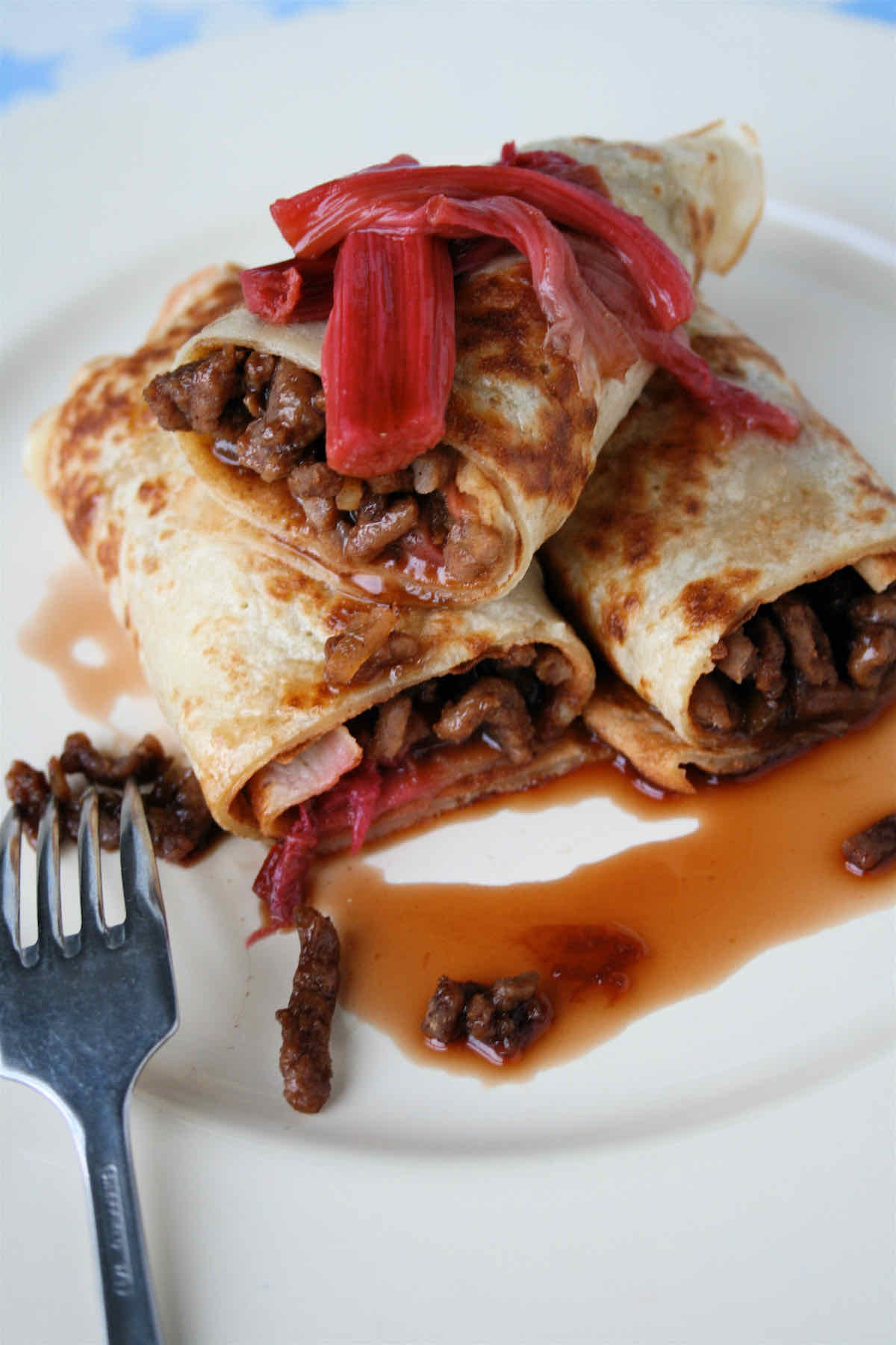 Spicy pork pancakes with rhubarb served in rolls with drizzle of sauce and extra cooked pink rhubarb on top.