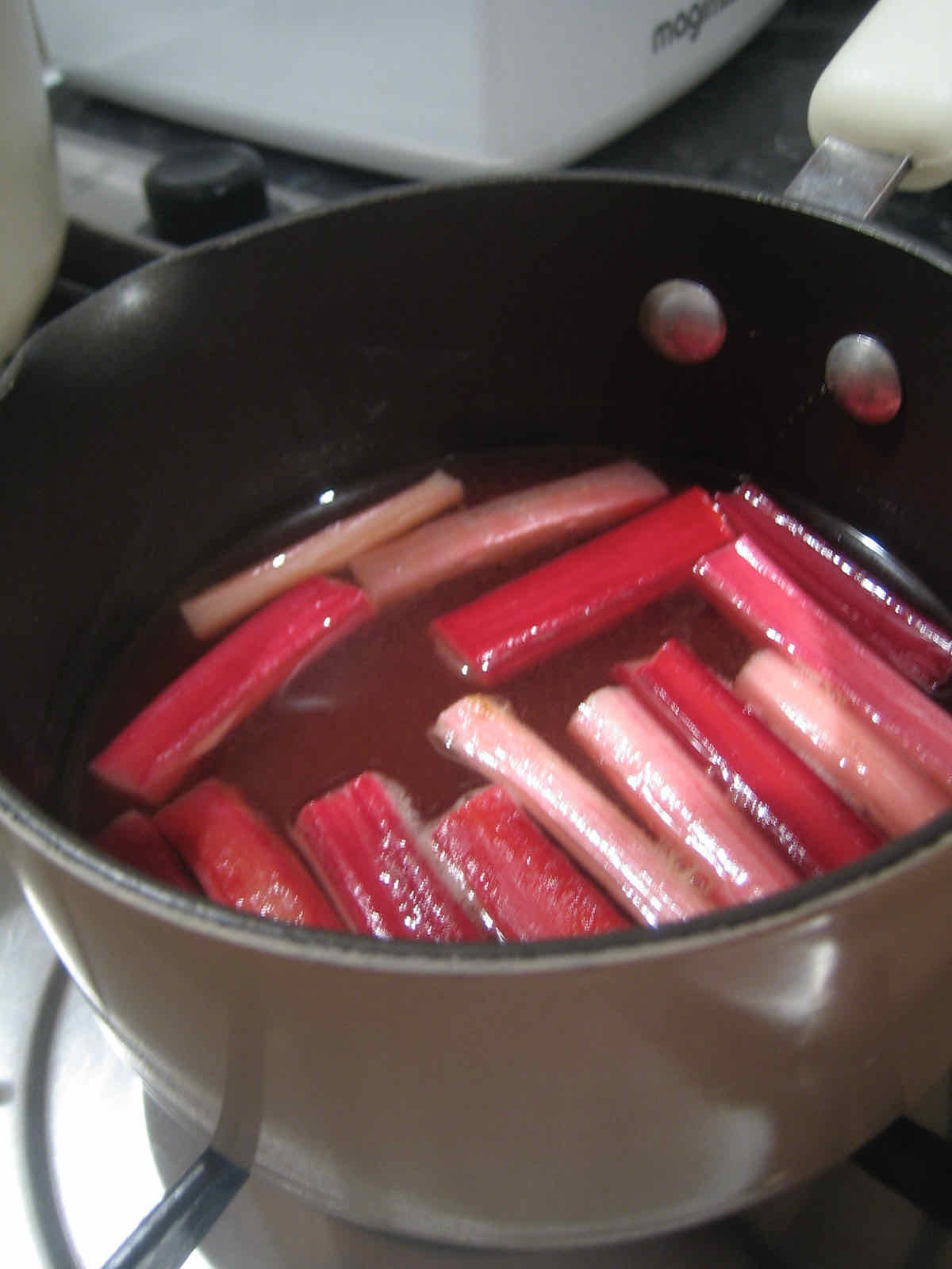 Pink sticks of rhubarb simmering in a saucepan