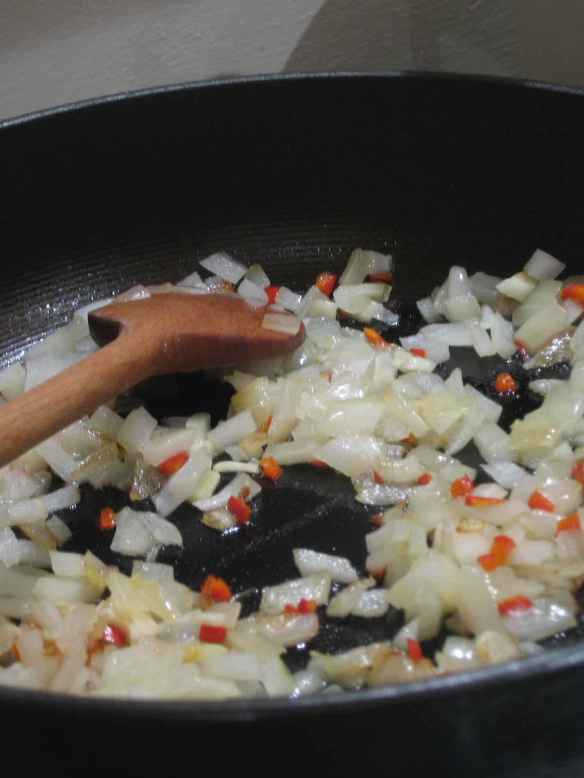 Finely chopped onion being fried in a pan with wooden spoon.