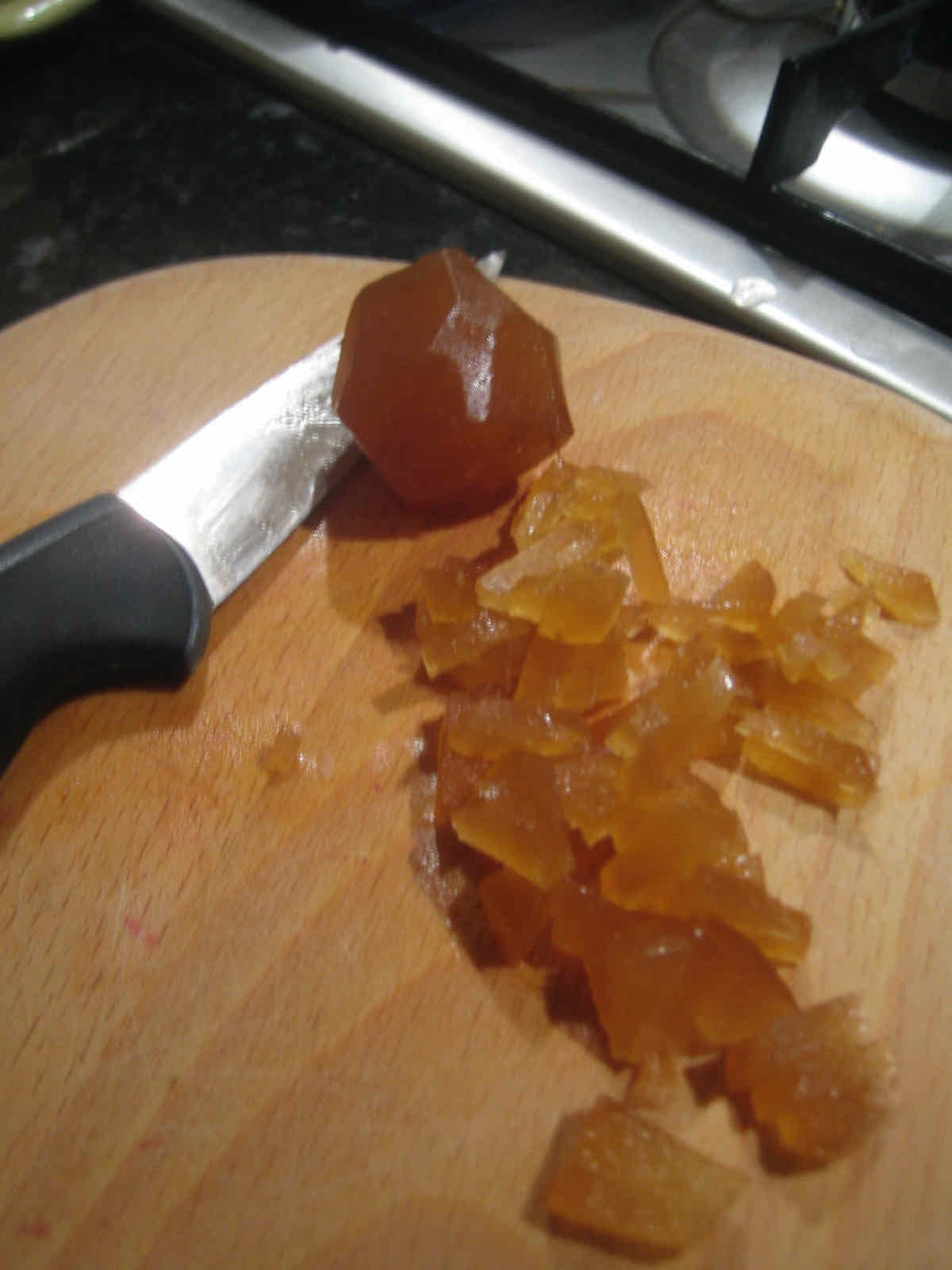 Crystallised stem ginger being chopped finely on a wooden board.