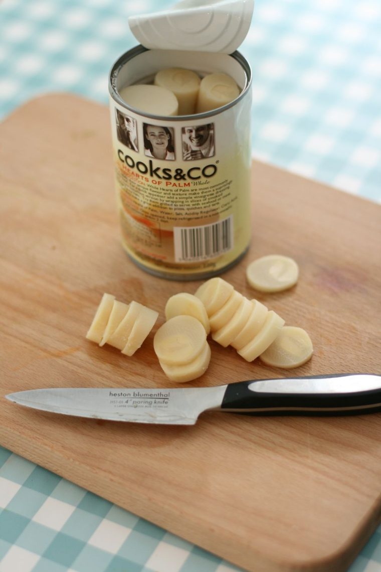 Open can of Cooks & Co hearts of palm, a few slices on a chopping board with knife