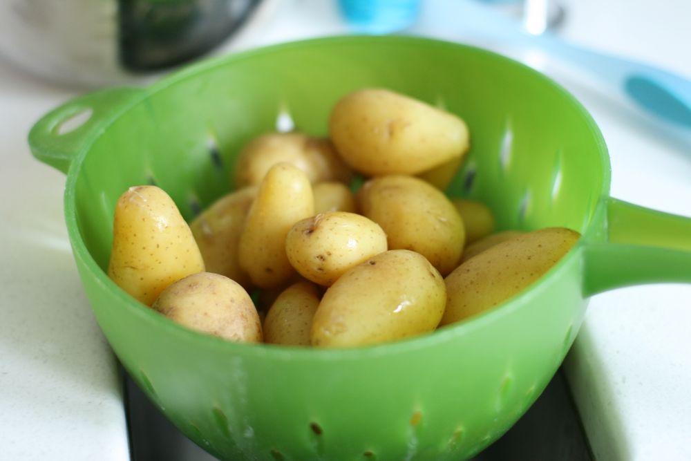 Boiled new potatoes with yellow skins being drained in a bright green plastic colander