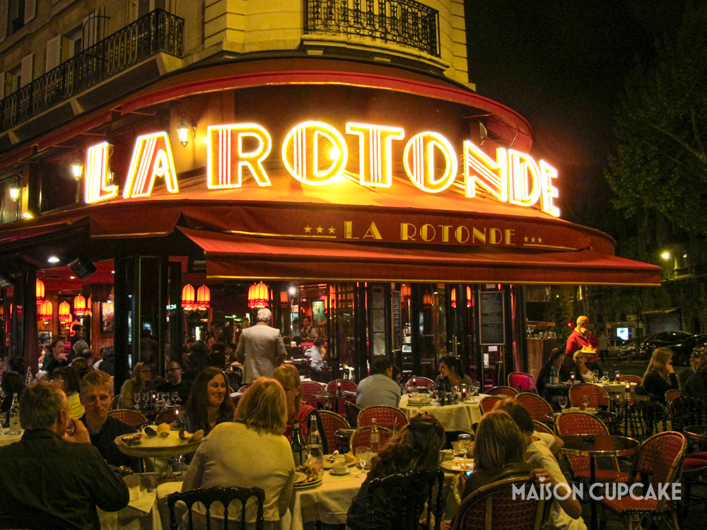 Paris La Rotonde by night with neon signage and diners eating.