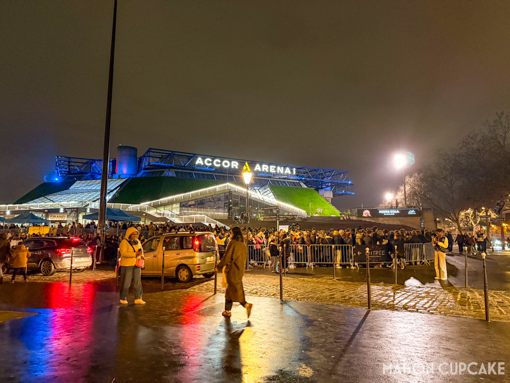 Paris Bercy Arena by night with crowds queuing for a concert.